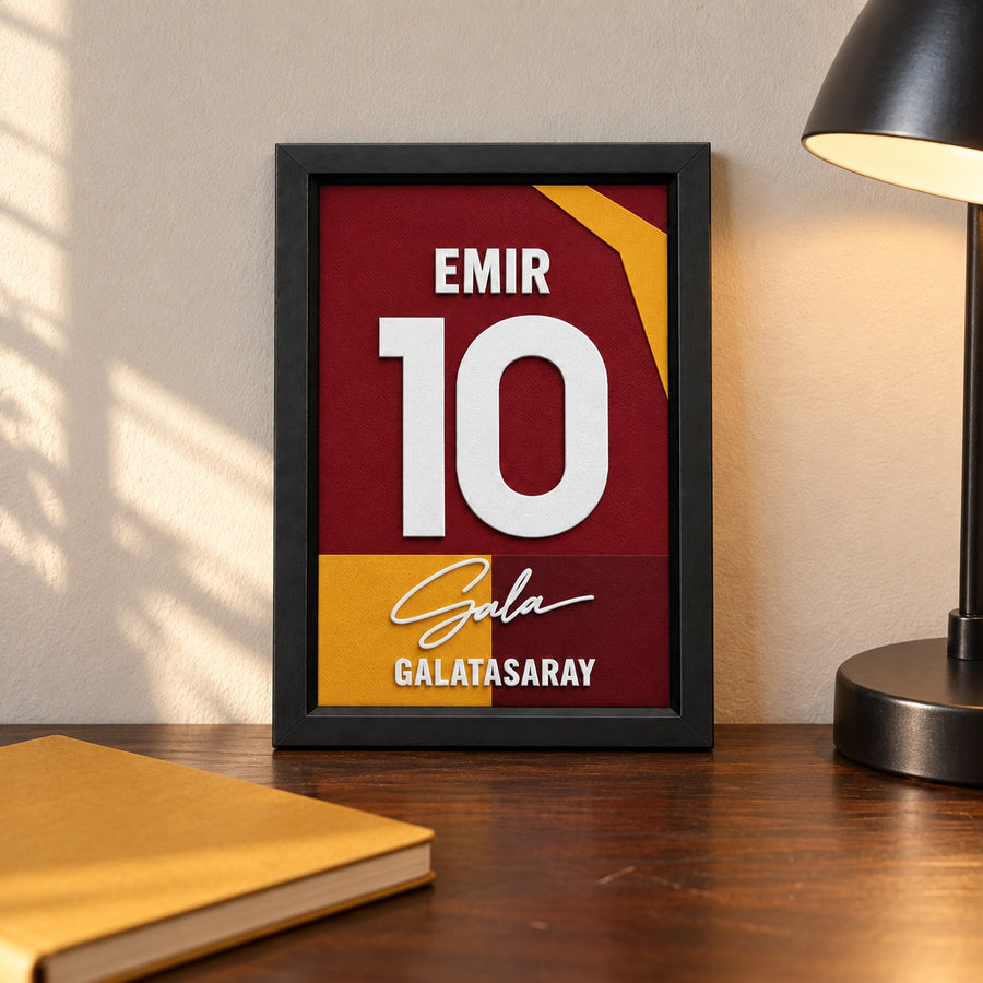 Galatasaray jersey frame personalized with EMIR and the number 10, standing on a desk beside a black lamp and a mustard notebook.