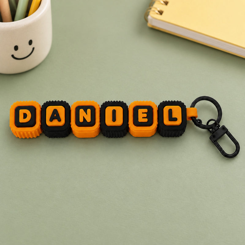 Orange and black DANIEL letter-block clicker with a black keychain attachment in a styled home setting.