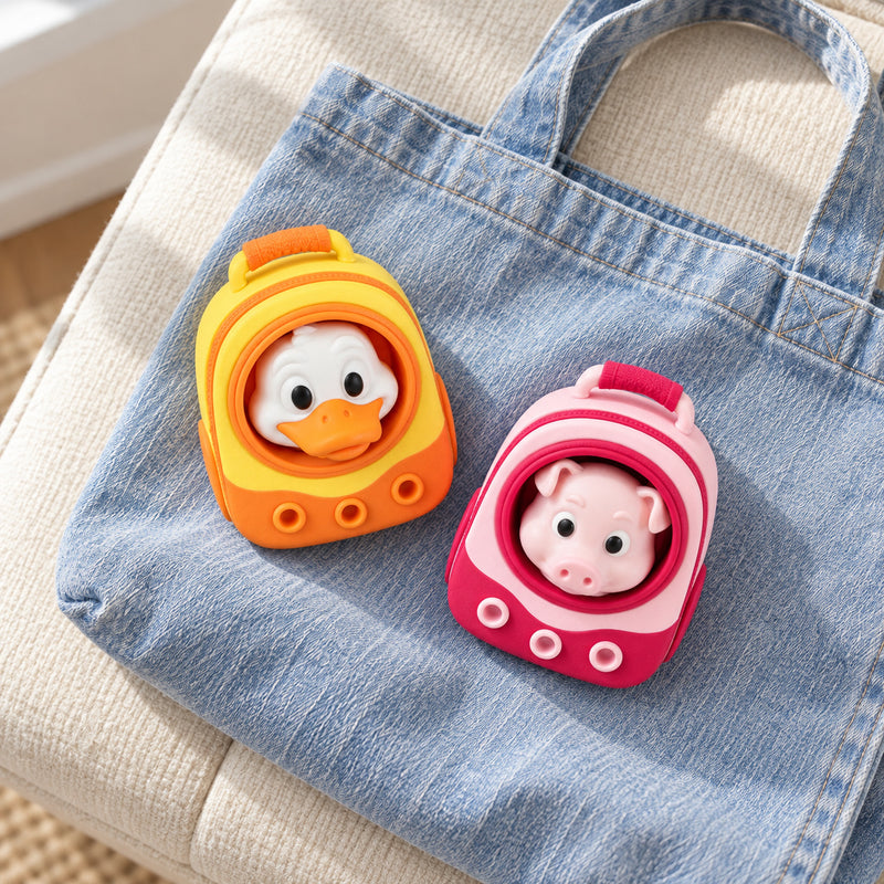 Yellow duck and pink pig backpack clickers resting on a denim tote.