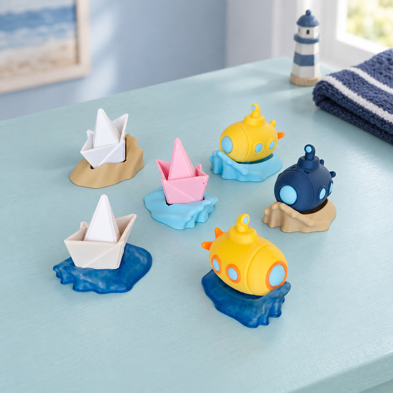 Miniature white and pink sailboats and colourful submarines on wave-shaped bases in a styled home setting.