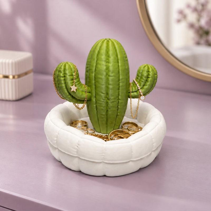 Green cactus jewellery stand in a white dish holding small jewellery pieces in a styled home setting.