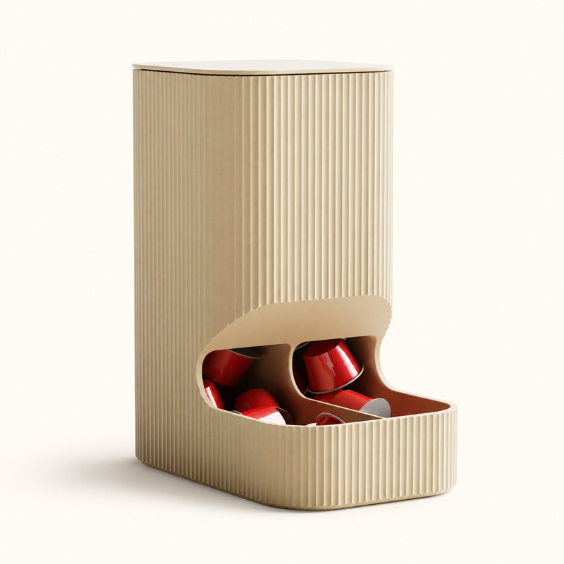 Beige fluted coffee capsule dispenser with red capsules visible in its lower opening on a soft white background.