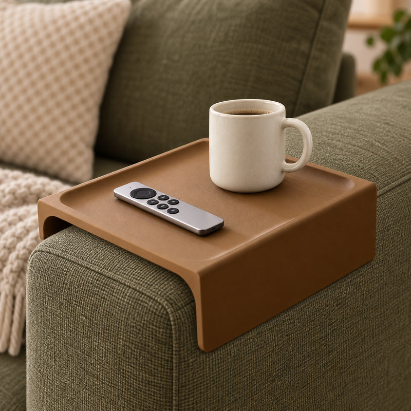 Brown couch armrest tray resting over an olive sofa arm with an ivory mug and a silver remote.