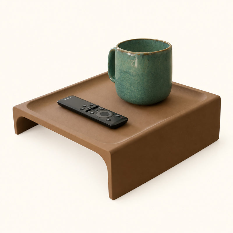 Brown couch armrest tray with a green mug and black remote on a soft white background.