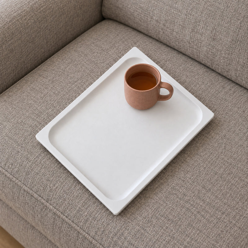 White rectangular tray on a grey sofa seat cushion with a terracotta mug in a styled home setting.