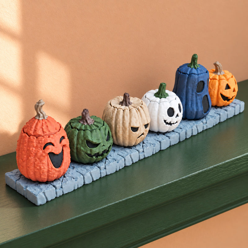 Six pumpkin designs on their base resting on a green shelf.