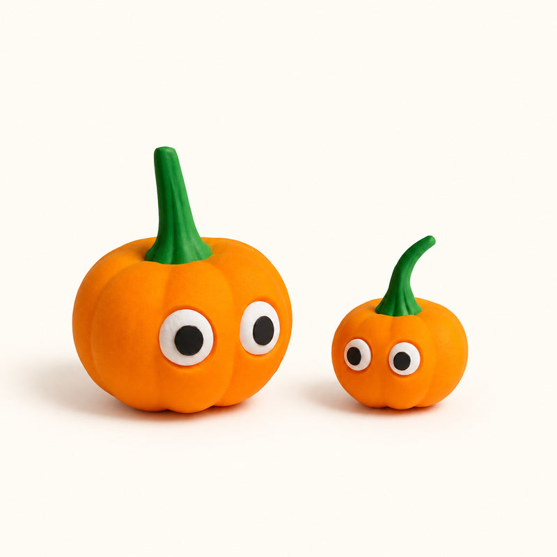 Two orange wide-eyed pumpkin decorations with green stems on a soft white background.