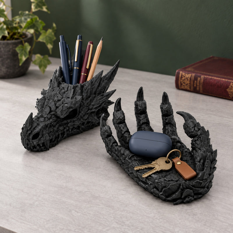 Black dragon desk organizer holding navy and burgundy pens, a pencil, brass keys and a blue earbud case on a grey desk.