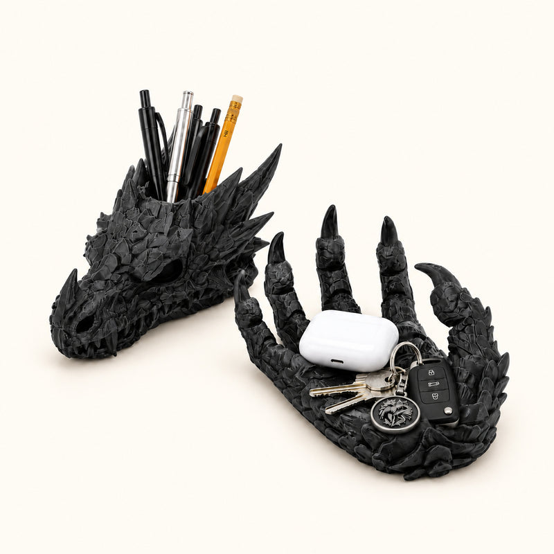Black dragon-head pen holder and claw-shaped catchall holding stationery, keys and a white earbud case on a soft white background.