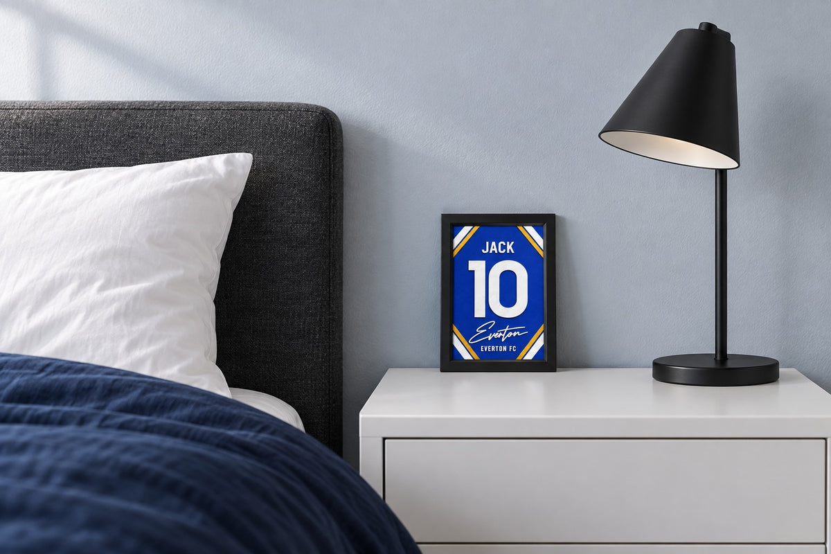 Everton jersey frame personalized with JACK on a bedside table beside a black lamp and a navy duvet.