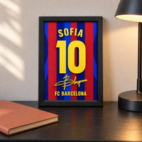 Barcelona jersey frame personalized with SOFIA and the number 10, standing on a desk beside a black lamp and an orange notebook.