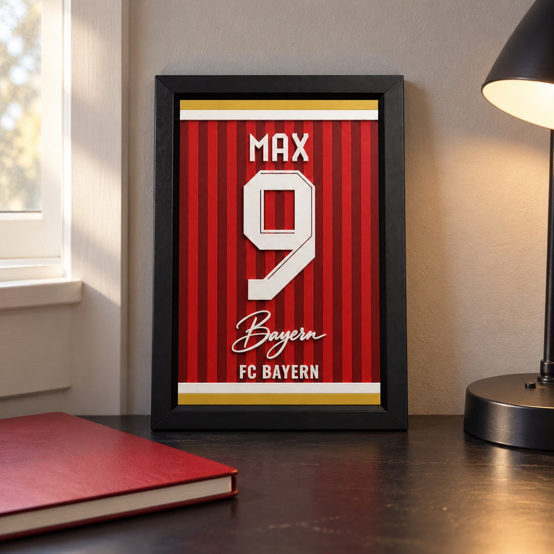 Bayern Munich jersey frame personalized with MAX and the number 9, standing on a desk beside a black lamp and a red notebook.