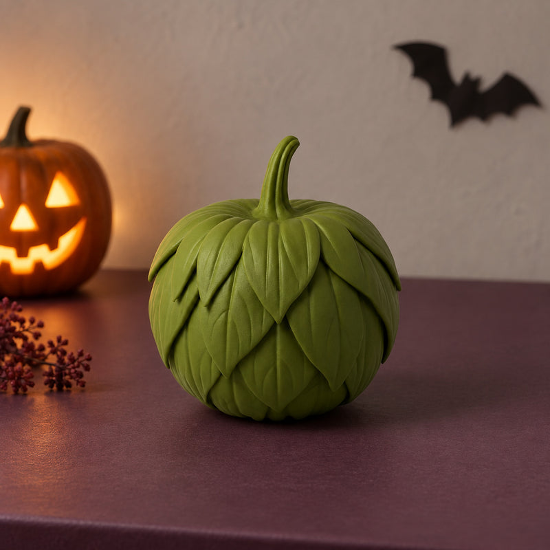 Green pumpkin decoration covered in overlapping sculpted leaves in a styled home setting.