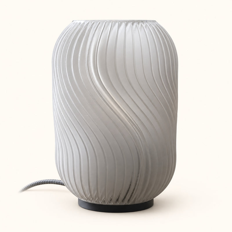 Pale upright table lamp with twisting vertical flutes and a visible cable on a soft white background.