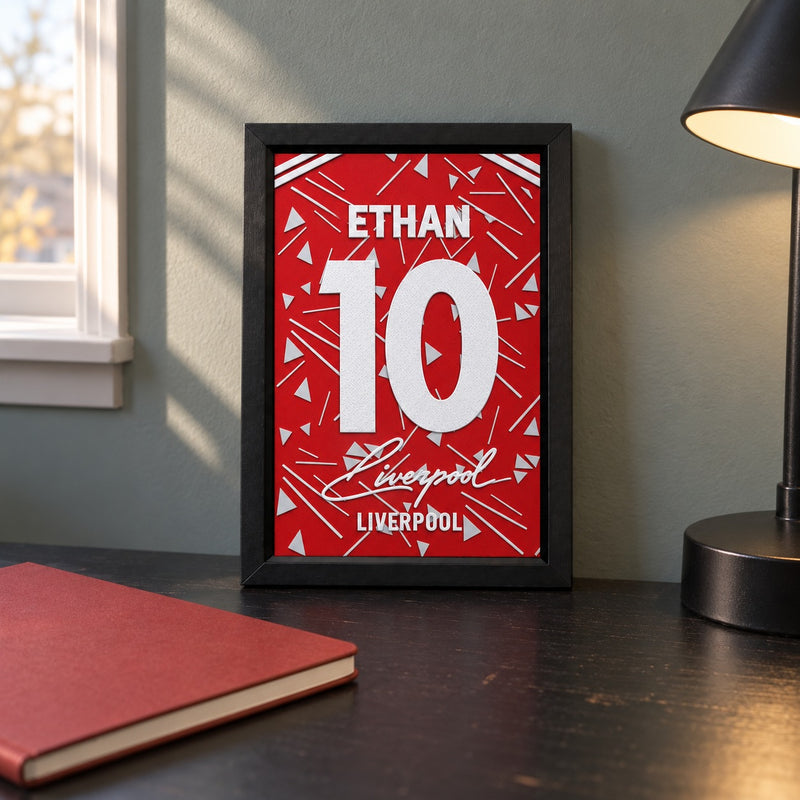 Liverpool jersey frame personalized with ETHAN and the number 10, standing on a desk beside a black lamp and a red notebook.