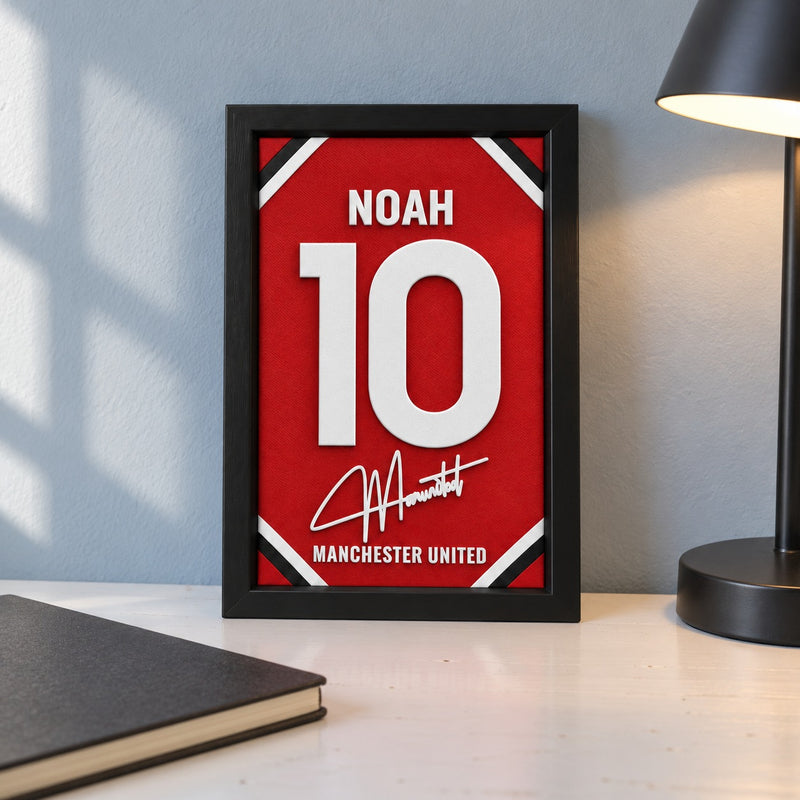Manchester United jersey frame personalized with NOAH and the number 10, standing on a desk beside a black lamp and a black notebook.
