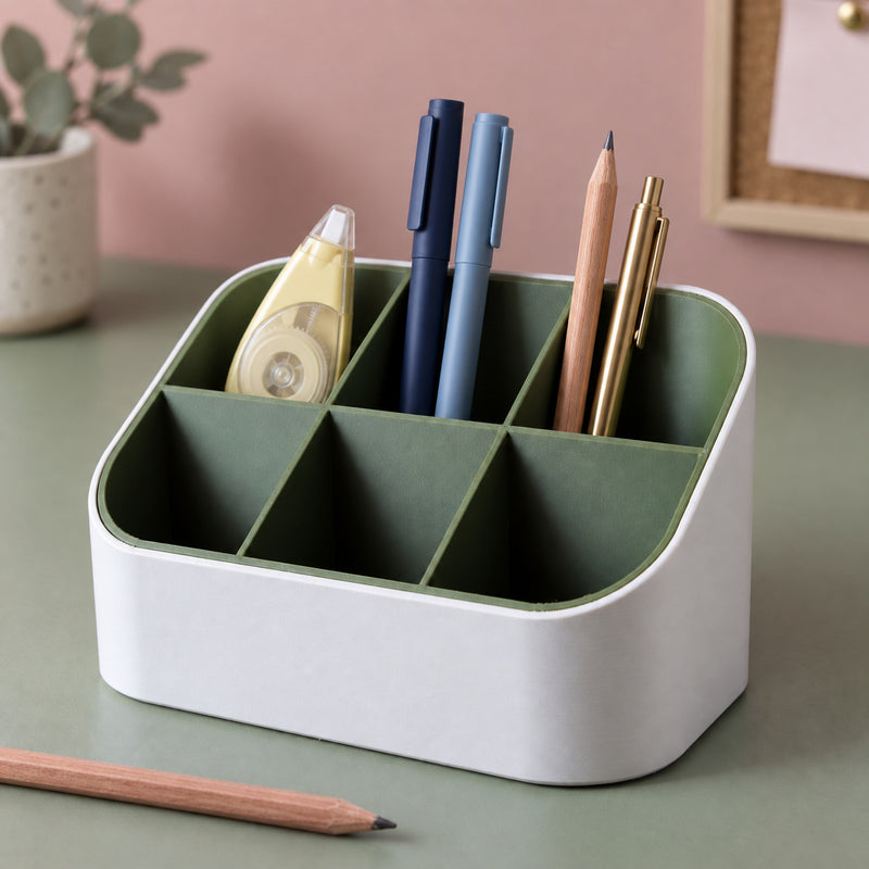 White and green six-compartment desk organizer holding blue pens, a pencil, a brass pen and correction tape in a styled home setting.