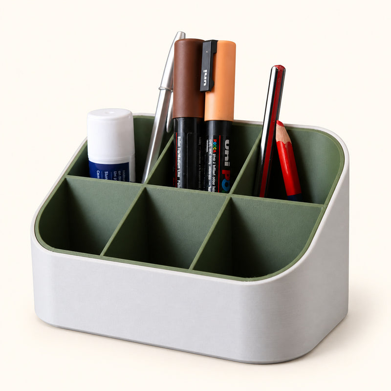 White and green six-compartment desk organizer holding pens, a pencil and a glue stick on a soft white background.
