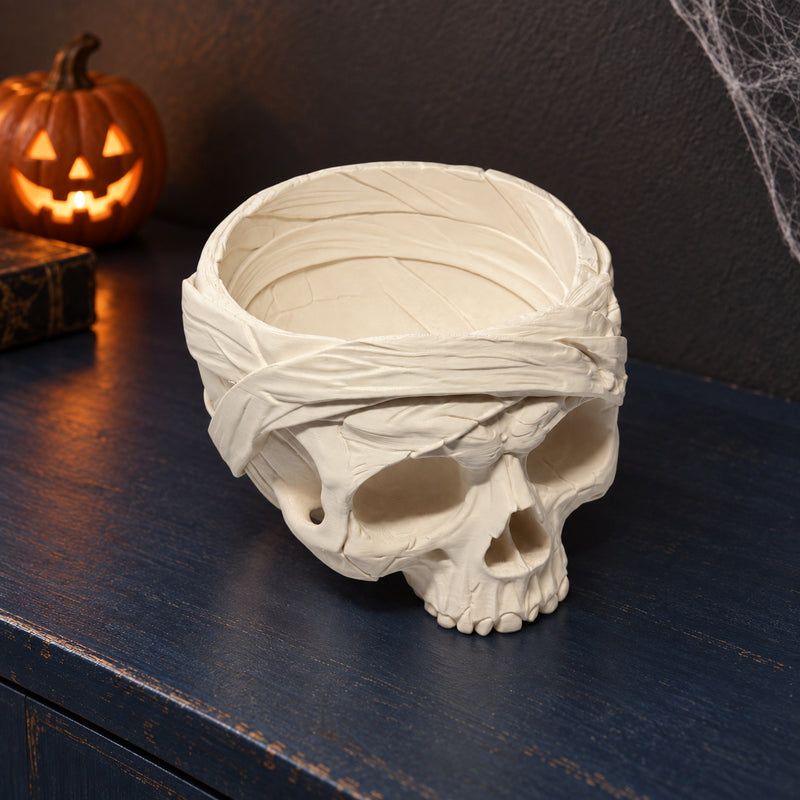 Pale skull bowl with sculpted bandage wraps and an open top in a styled home setting.