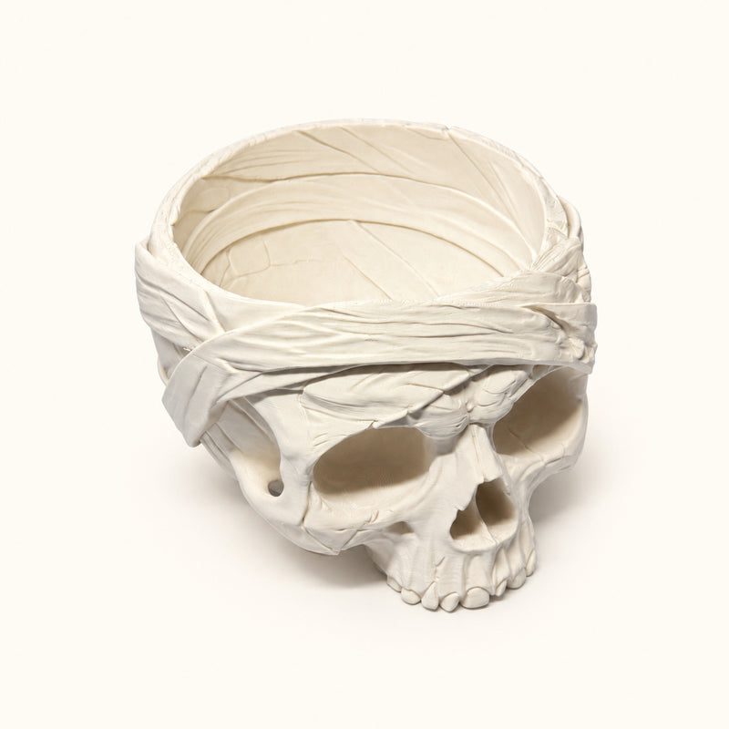 Pale skull bowl with sculpted bandage wraps and an open top on a soft white background.