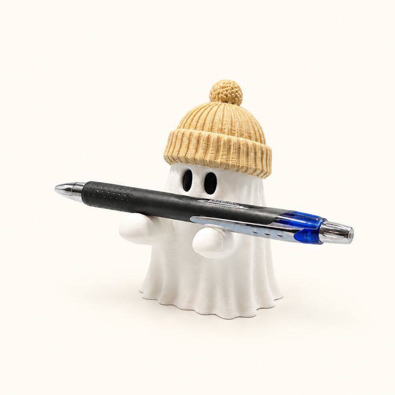 White ghost pen holder wearing a beige toque and supporting a black and blue pen on a soft white background.