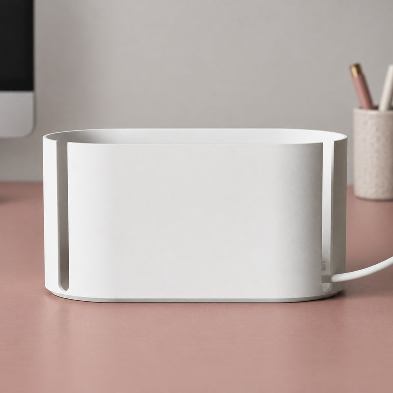 White rounded cable management box with narrow side slots and a cable in a styled home setting.
