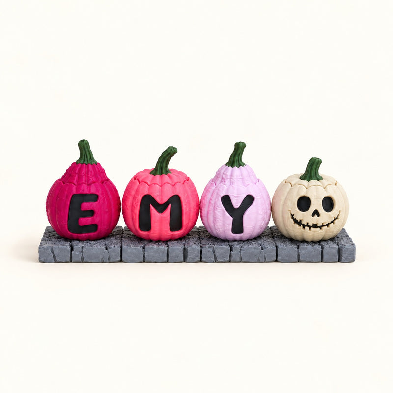 Four pumpkin clickers spelling a name in raised letters, on a grey stone base.