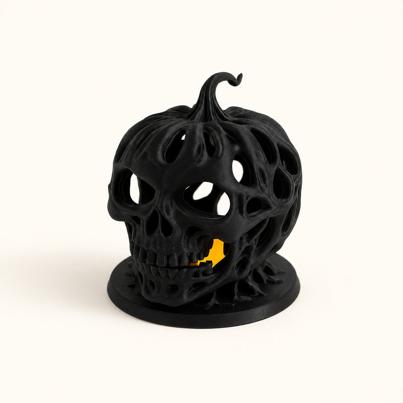 Black openwork skull pumpkin lantern with irregular holes and a warm glow on a soft white background.