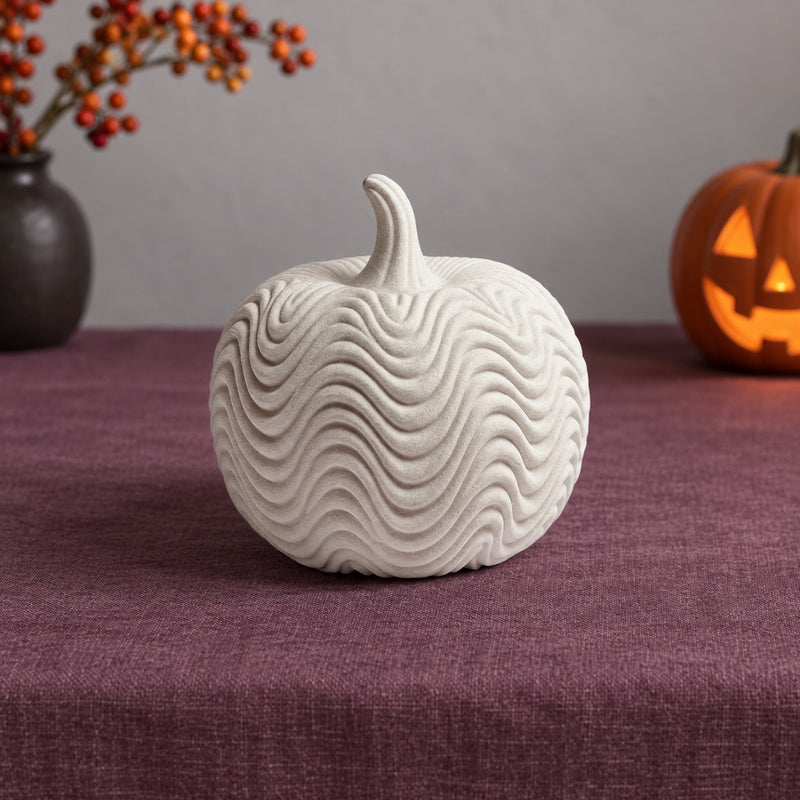Pale pumpkin decoration with flowing wave-pattern ridges in a styled home setting.