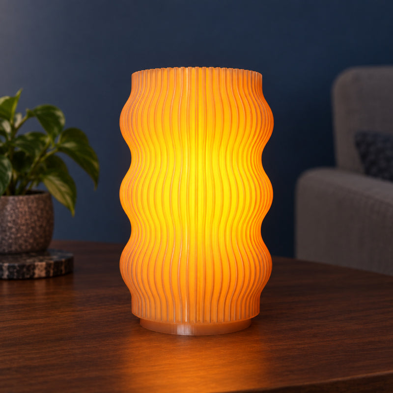 Wavy ribbed table lamp glowing amber in a styled home setting.