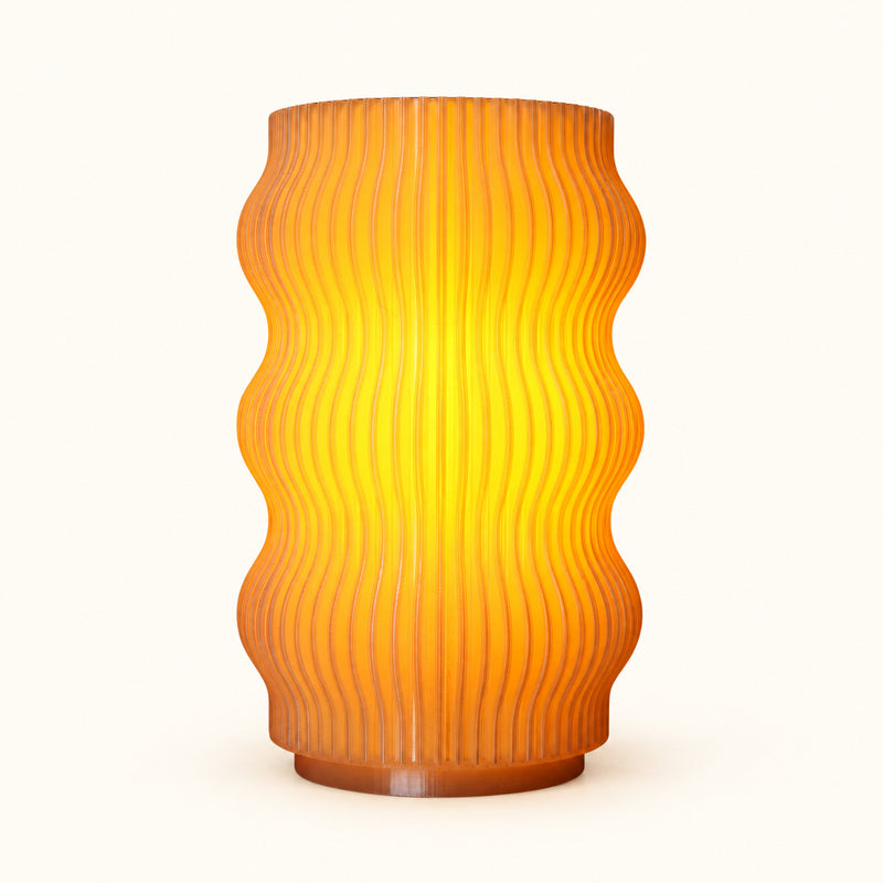 Wavy ribbed table lamp glowing amber on a soft white background.