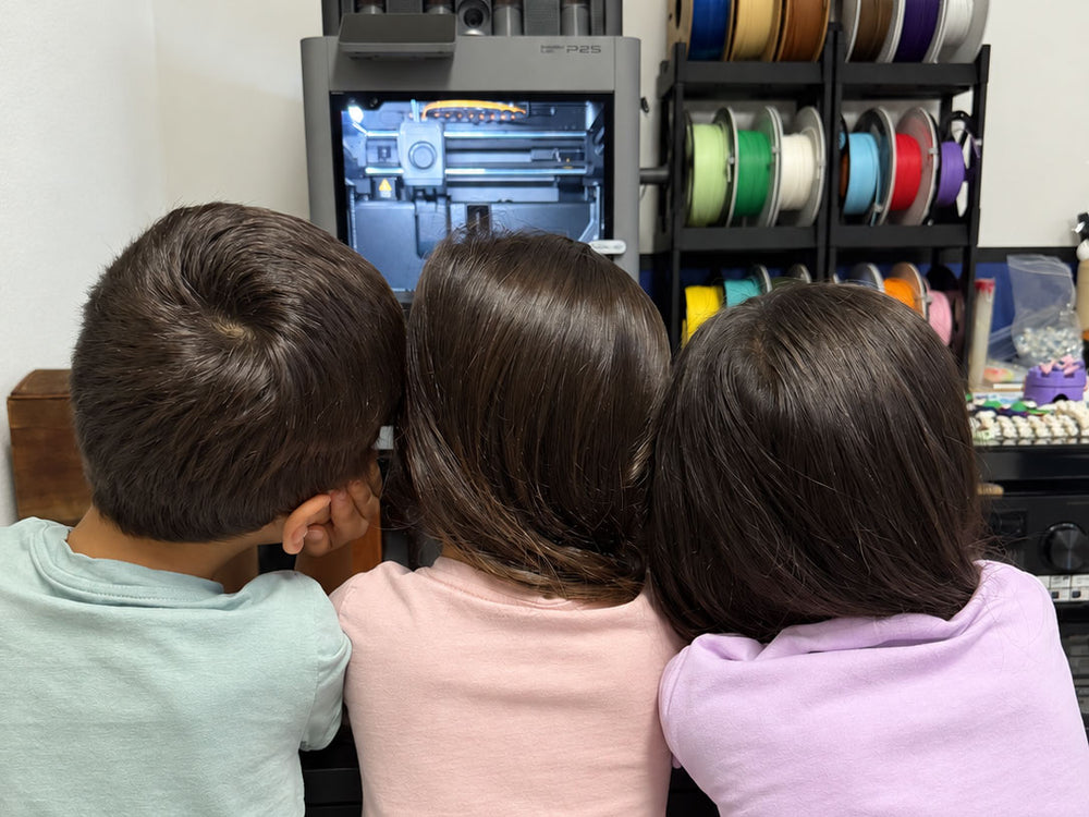 Three children watching a 3D printer at the We Are Three home workshop.