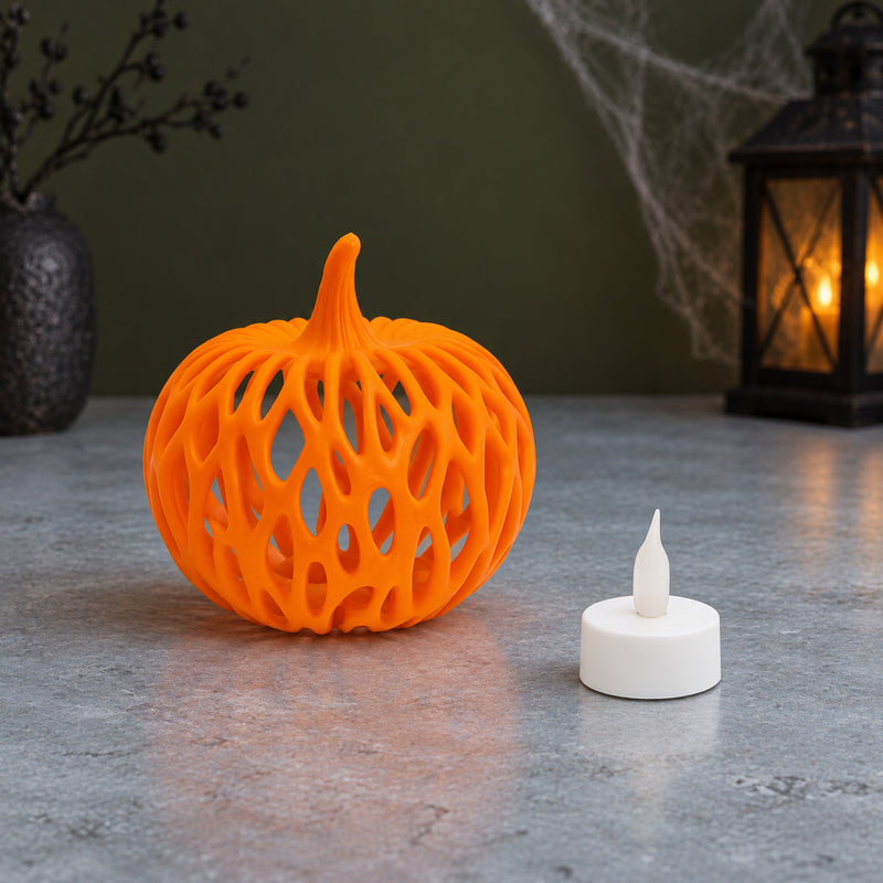 Orange pumpkin with looping woven-style openings beside a white LED tealight in a styled home setting.
