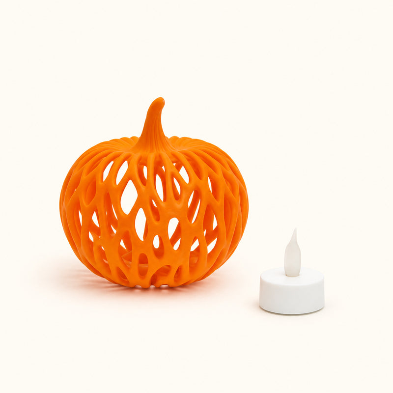 Orange pumpkin with looping woven-style openings beside a white LED tealight on a soft white background.